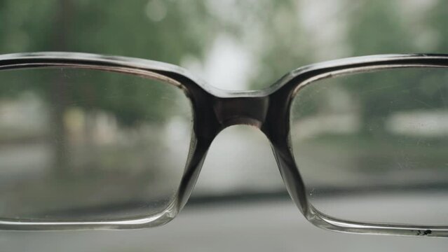 Driver of a car with poor eyesight. The driver raises his head, silhouettes of passing cars are visible through the glasses. Blurred image.