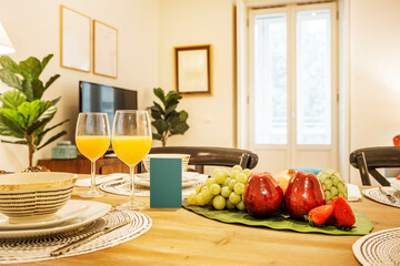 Apartment decorated in pastel colors with a breakfast table with assorted fruits, white grapes, custard apples, red apples, strawberries and juices in crystal glasses
