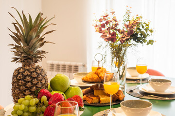 Centerpiece with tray of fresh fruit, bunch of grapes, lots of muffins and candies, decorative vase, green apples, strawberries, croissants, ripe plums and glasses of orange juice