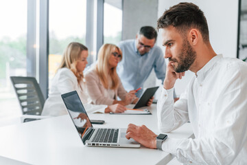 Portrait of young man that sitting by the table. Group of professional business people is in the office