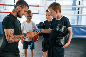 Preparing for the sparring. Young tattooed coach teaching the kids boxing techniques