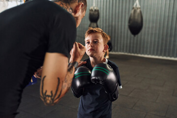 Teaching how to punch. Coach is with boy showing box techniques indoors