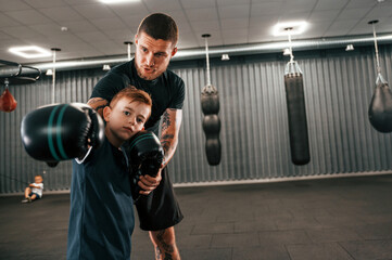 Giving advices. Coach is teaching the boy box techniques indoors