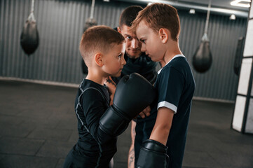 Pre fight preparing. Looking at each other. Young tattooed coach teaching the kids boxing techniques