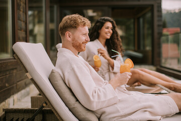 Young couple relaxing on beds and drinking fresh orange juice on the outdoor terrace