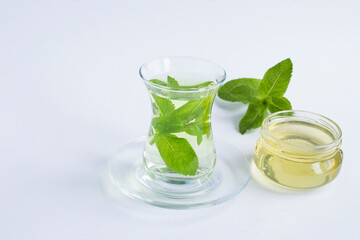 Tea with mint and honey in the glass cup on the white background. Closeup. Copy space.