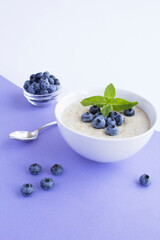 Oatmeal with milk and blueberry in the white bowl on the purple background. Healthy breakfast. Location vertical.