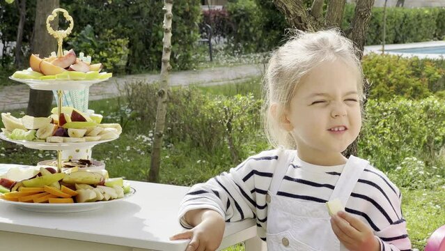 Little girl eats a piece of apple sitting at the table