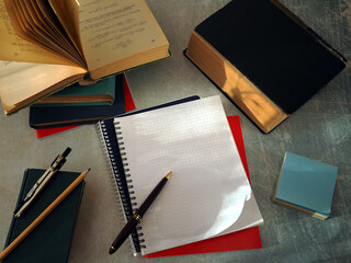 Open books and notebooks lie on the table. There is a pen on a clean notebook page. The concept of...