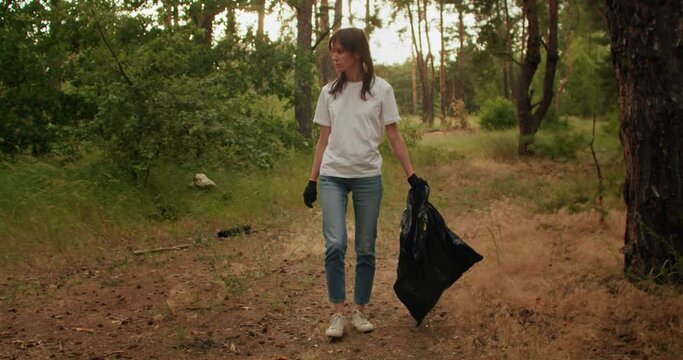 People cleaning up the forest and collecting trash, a woman is picking up a plastic bottle