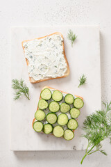 Obraz na płótnie Canvas Cooking traditional English tea sandwiches with cucumber, cream cheese, dill for breakfast on white marble board. View from above. Vertical format