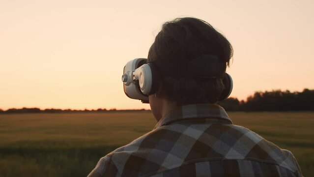 Farmer in virtual reality helmet in front of a sunset agricultural landscape. Man in a countryside field. Country life, food production, farming and technology concept .