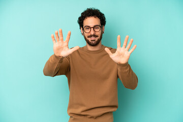 young bearded man smiling and looking friendly, showing number ten or tenth with hand forward,...