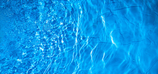 Photo of water in a blue pool. Background of clear blue water. Refreshing freshness of water.A rectangular banner with a splash of water in the pool.