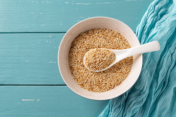Toasted sesame seeds and white spoon in a bowl over teal wooden background. Porcelain bowl full of roasted white til. Organic benne grains in asian cuisine. Sesamum indicum for healthy eating.