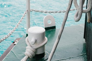 White thick rope lies on ship mooring bollard on pier. Boat drifts on rippling water. Mooring rope...