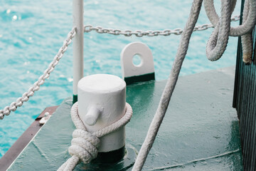 Fototapeta premium White thick rope lies on ship mooring bollard on pier. Boat drifts on rippling water. Mooring rope held by reef knot against metal chain closeup