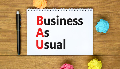BAU business as usual symbol. Concept words BAU business as usual on white note on a beautiful wooden background. Metallic pen. Business and BAU business as usual concept. Copy space.