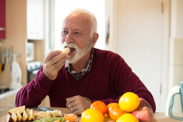 Senior man eating fruits in the kitchen on a sunny day