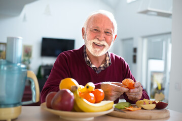 Senior man eating fruits in the kitchen on a sunny day - 522582460