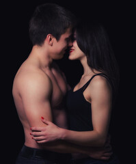 Young couple hugging and kissing as foreplay before having sex isolated on black background