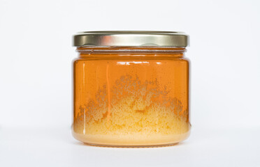 Jar of honey that is starting to crystalize on a white background