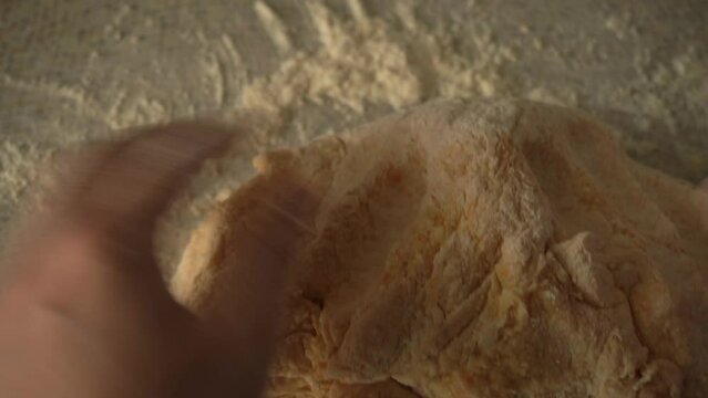 a large lump of dough from a pumpkin is carefully kneaded by female hands, close-up shooting. home kitchen. Handheld shooting