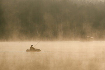 a fisherman in a boat catches fish in the early foggy morning and the forest in the distance