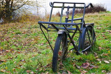 an old rusty blue cargo bike stands on an autumn meadow in front of a lake