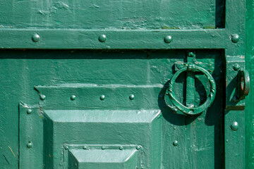 The metal gate is padlocked. Rusty padlock on the gate, close-up. Rough iron doors painted green.