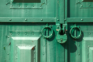 The metal gate is padlocked. Rusty padlock on the gate, close-up. Rough iron doors painted green.