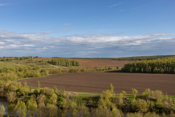 Fototapeta premium View of the countryside. bright greenery in the ravine. Saturated green grass against the blue sky. Plowed field on the horizon.