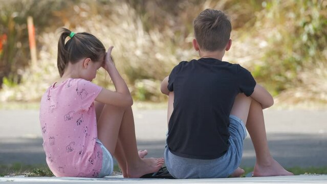 Two happy smiling teenage children, boy and girl sitting outdoors resting having fun on summer sunny day