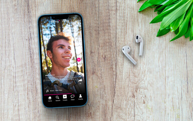 Sample social media app interface on mobile phone on a wooden table with headphones - concept of...