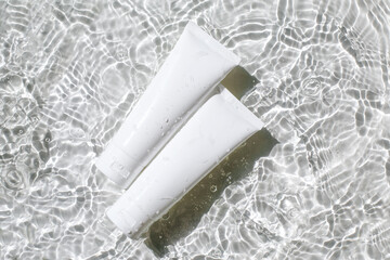 Tubes of cosmetic product with sunscreen from sunburn floating on surface of the water with rings and ripples. Beauty products for anti-aging care, moisturizing and cleansing.