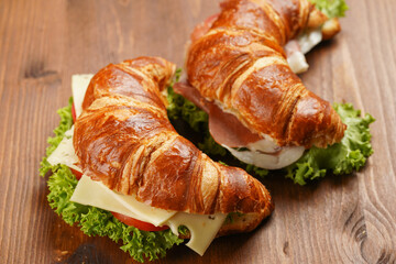 two lye croissant sandwiches with iberian ham, tomato slices, lettuce and cheese on marble board on wooden background