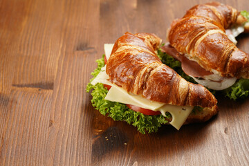 two lye croissant sandwiches with iberian ham, tomato slices, lettuce and cheese on marble board on wooden background