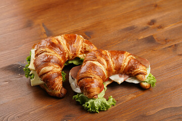 two lye croissant sandwiches with iberian ham, tomato slices, lettuce and cheese on marble board on...