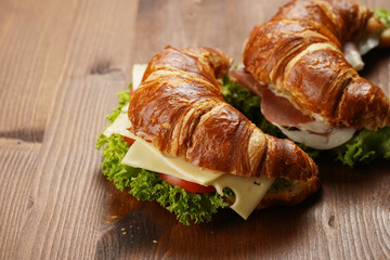 two lye croissant sandwiches with iberian ham, tomato slices, lettuce and cheese on marble board on wooden background