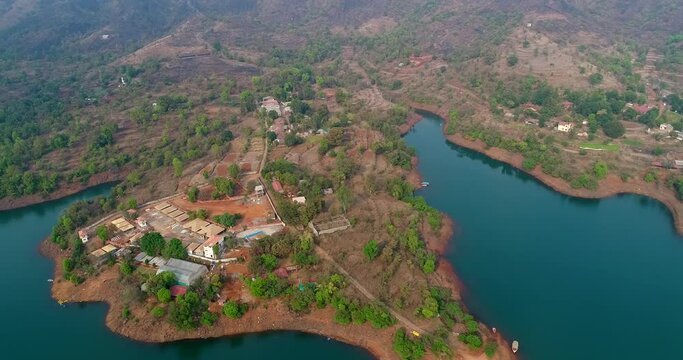 Aerial shot of river running along fields with reddish soil, houses around