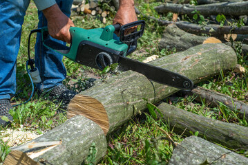 A male uses a chainsaw to cut up a log into firewood.