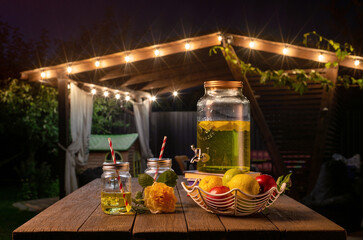 drink station with small bottles and homemade lemonade on wooden terrace with abstract night light bokeh of night festival in garden, copy space for display of product or object presentation