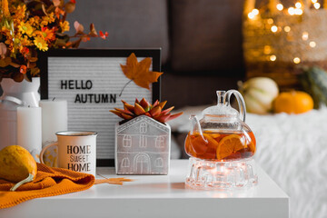 Cozy autumn concept. Home warmth in cold weather. Still-life. A blanket, pumpkins, a teapot and a cup of tea on the coffee table in the home interior of the living room. - obrazy, fototapety, plakaty