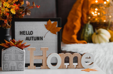 Cozy autumn concept. Home warmth in cold weather. Still-life. A blanket, pumpkins, flowers and the inscription home on the coffee table in the home interior of the living room. - obrazy, fototapety, plakaty