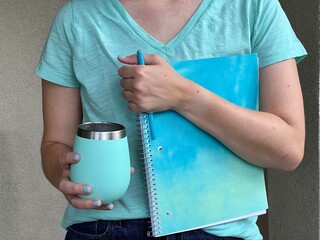 Teen female student holds color coordinating agua blue composition book, cup and pen