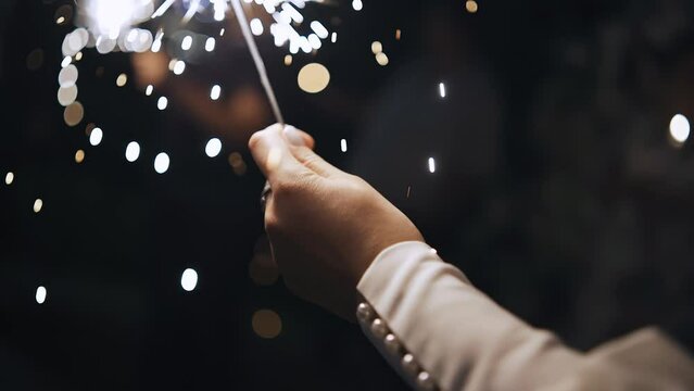 A girl and a guy are holding a burning sparkler in their hands. Close-up shooting in slow motion