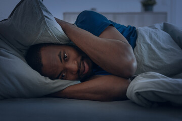 Black Man Having Insomnia Covering Ears With Pillow In Bedroom