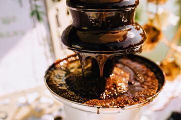 Hot brown milk melted chocolate pours over the tiers of the fountain close-up. Food photography.