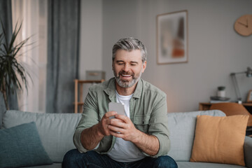 Glad elderly european man with beard chatting on smartphone, watching video, playing game