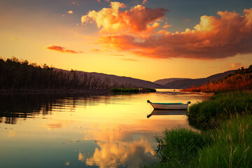 Krajobraz wodny. Widok na jezioro i zachód słońca. Piękny zachód słońca nad jeziorem ze starą łodzią i bezchmurnym niebem w tle, Polska - obrazy, fototapety, plakaty